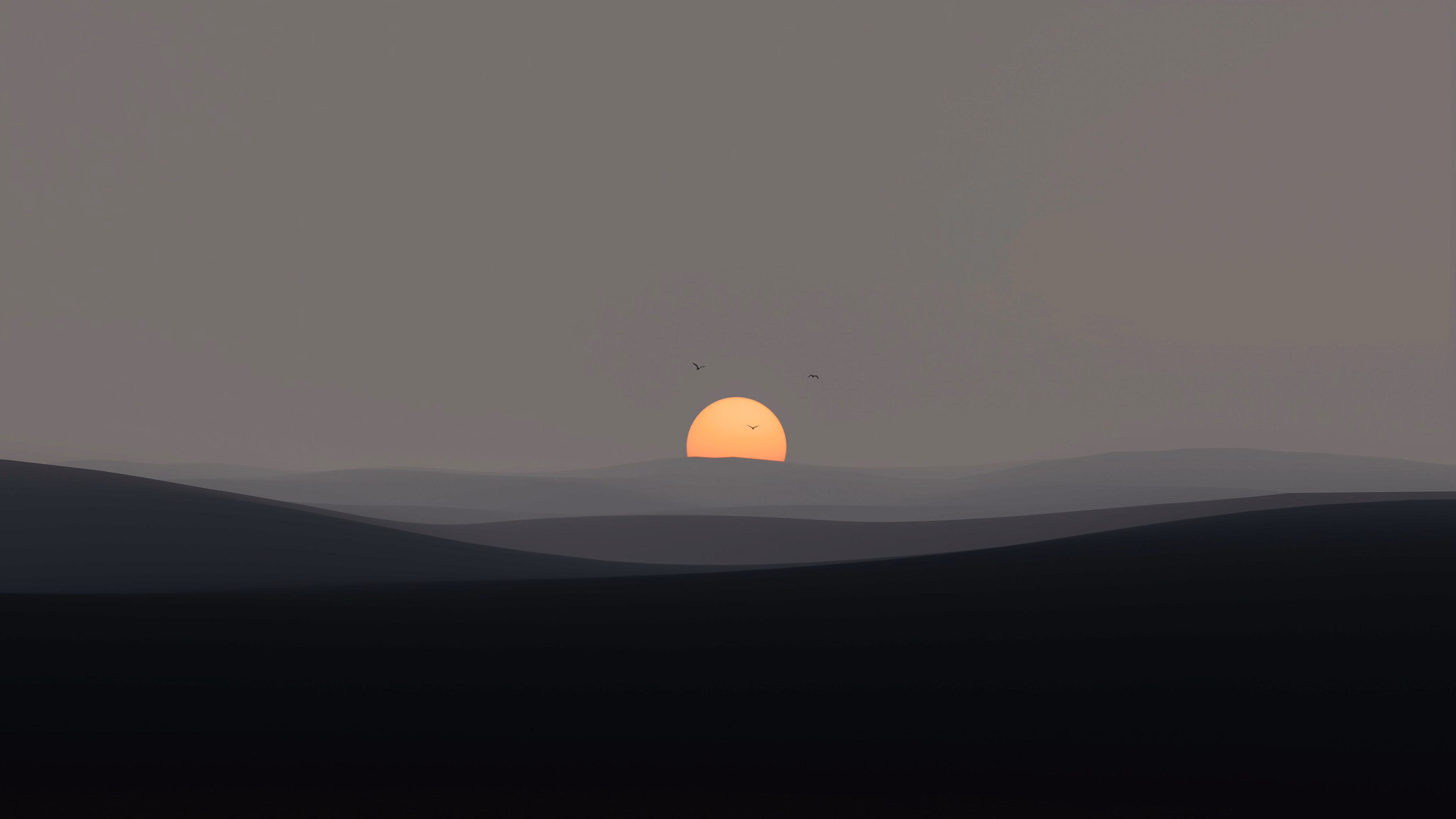 A soft orange sun setting behind layered grey hills